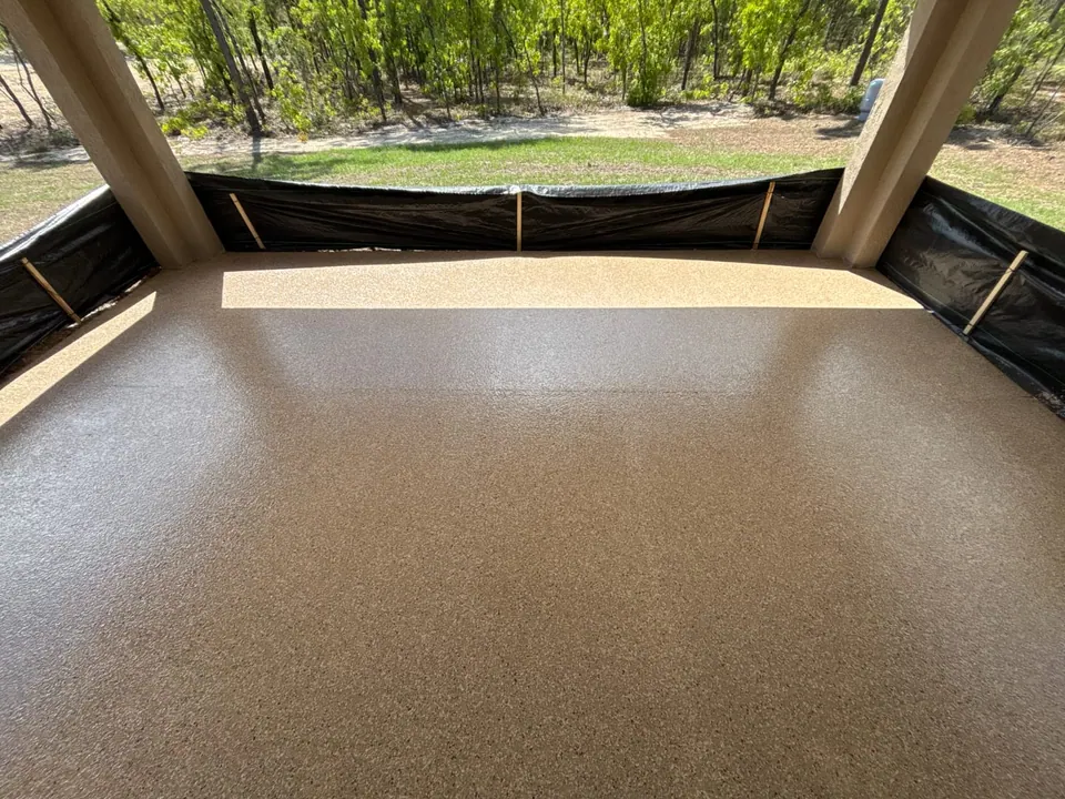 Tan flake floor coating on a covered patio overlooking a wooded yard