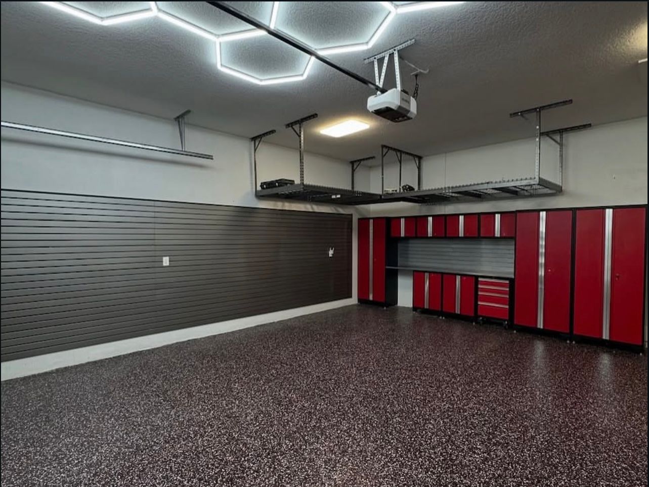 Garage with hex lighting, overhead storage racks, red cabinets, and coated floor